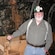 Bearded man with suspenders and miners hat stands in front of rusted mining equipment in a cave